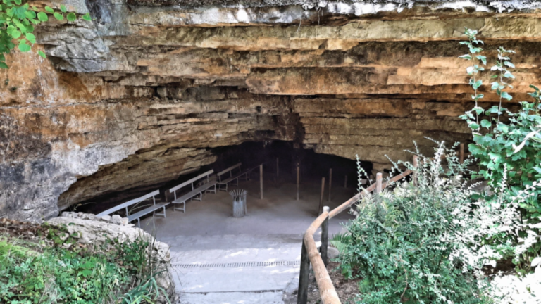 Entrée aménagée des Grottes de Bèze sous une large voûte calcaire, avec ses bancs et sa rambarde en bois